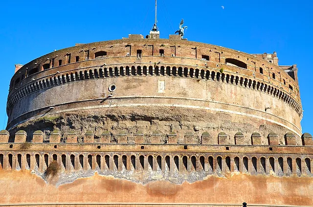 Close view of the huge round drum of Castel Sant'Angelo, Hadrian's old mausoleum, with its rows of small arches and the battlemented outer wall in front, under a blue sky