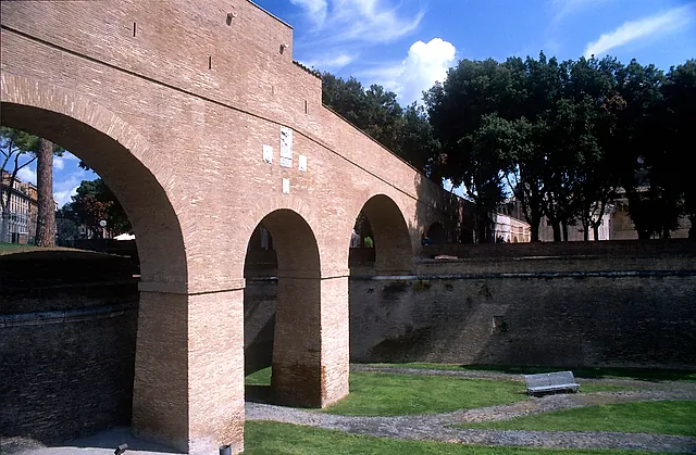 The Passetto di Borgo, the raised brick corridor linking the castle to the Vatican, crossing the grassy dry moat on tall arches among trees and a blue sky