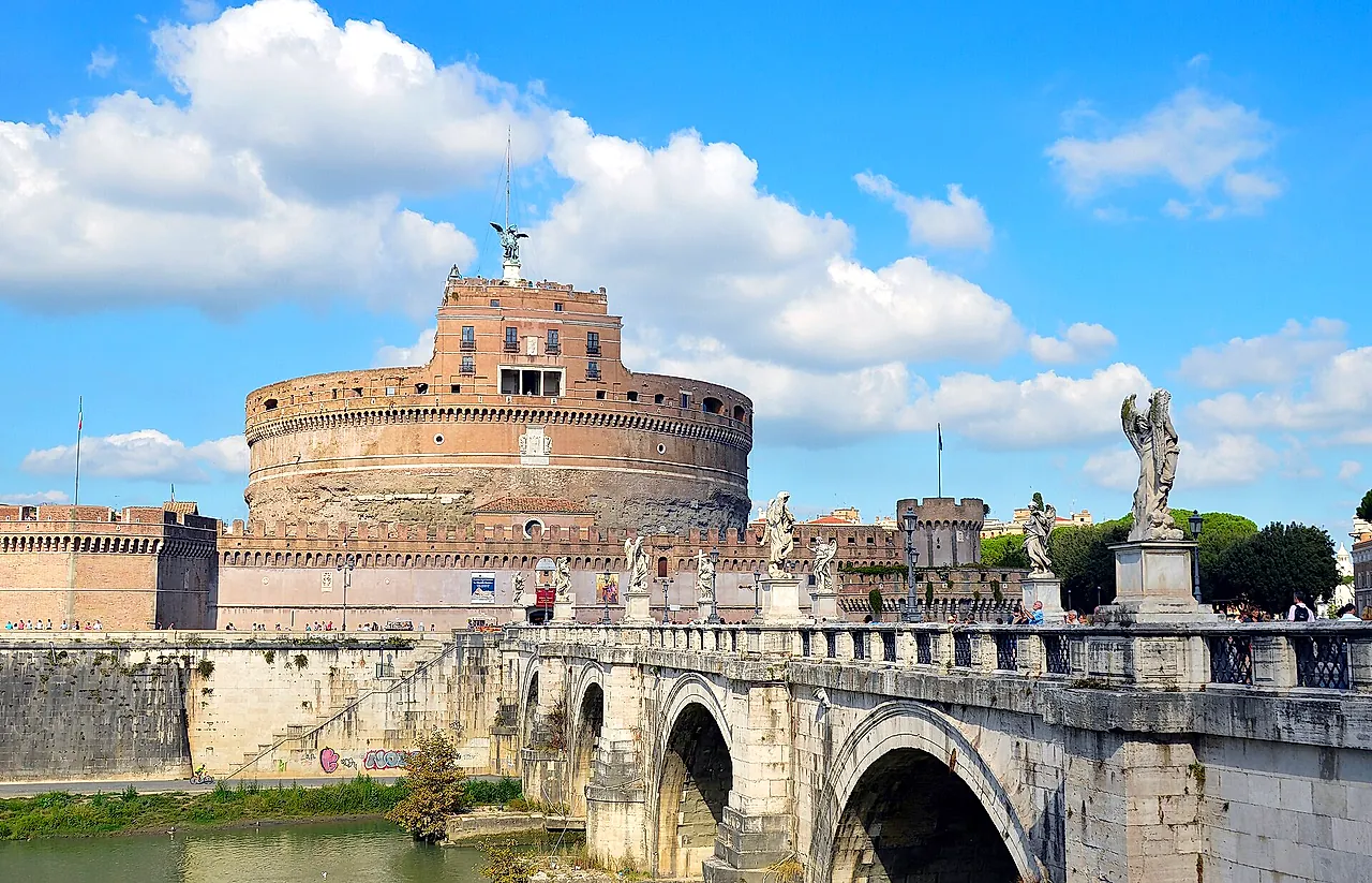 The Ponte Sant'Angelo leading to Castel Sant'Angelo on a bright day, with white clouds in a blue sky and some of the marble angels along the bridge parapet